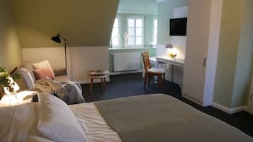 A hotel room with a bed, a desk, a chair, a lamp, and a television.