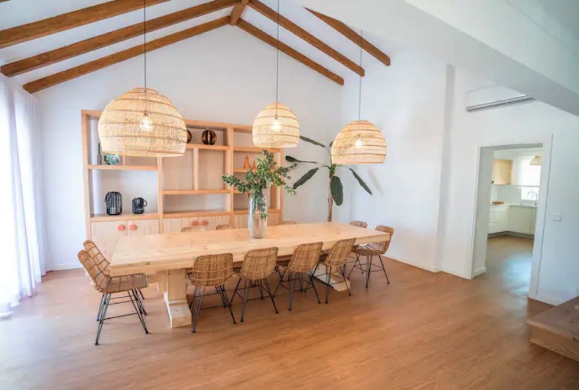 A dining area with a long wooden table, six wicker chairs, and three hanging light fixtures.