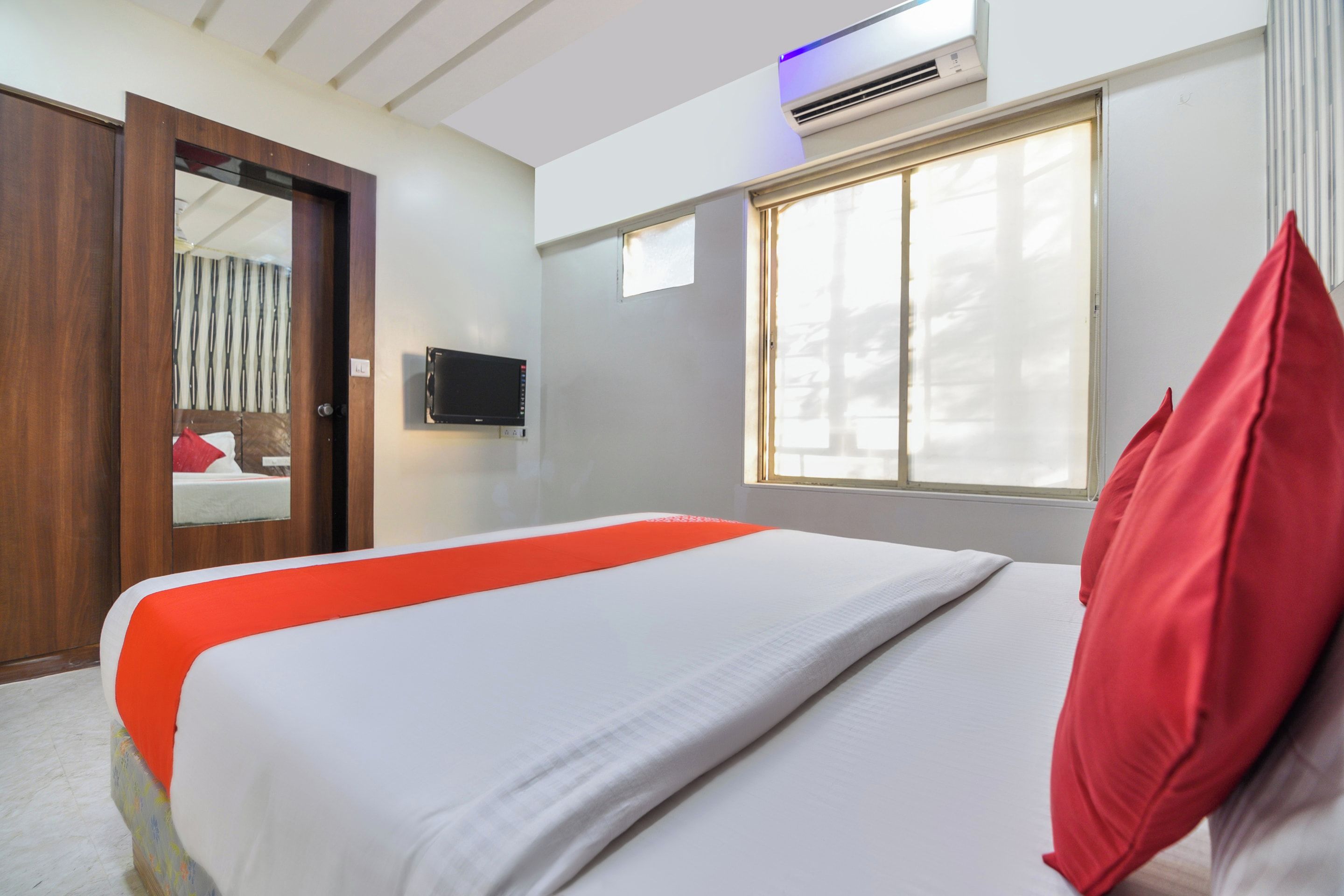 A hotel room with a bed, a television, a window, and a door.