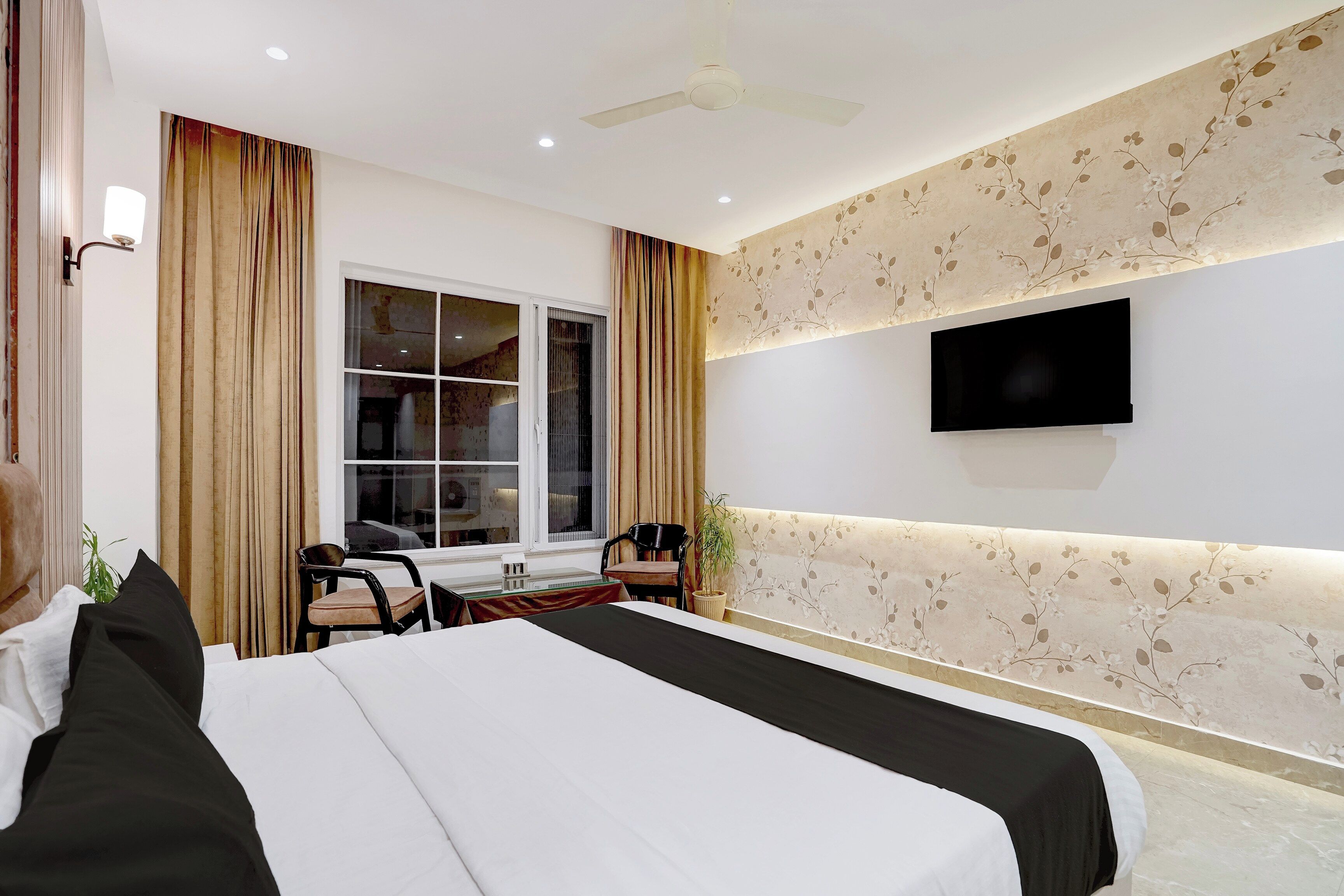 Habitación de hotel con cama, escritorio, sillas, televisor y ventana con cortinas.