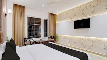 Habitación de hotel con cama, escritorio, sillas, televisor y ventana con cortinas.