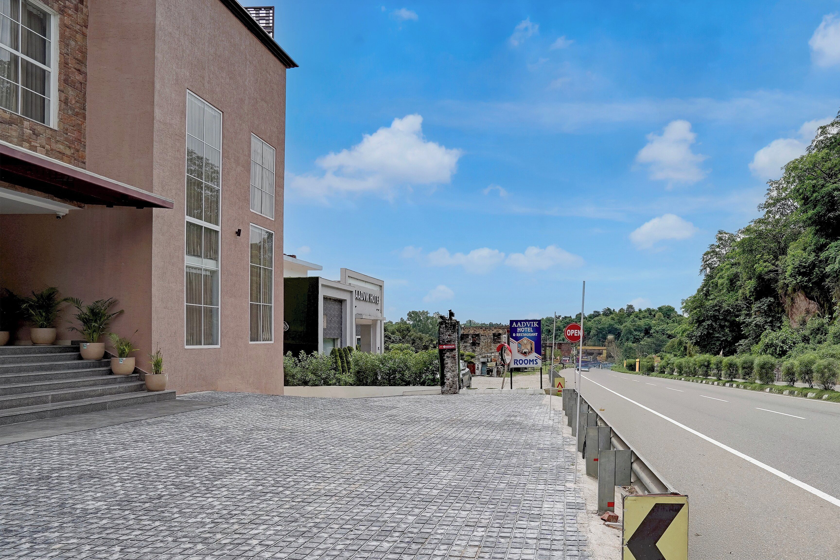 A hotel entrance with a paved driveway leading to a road, a clear sky, and greenery in the background.