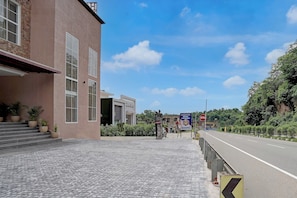 Entrada de hotel con un camino pavimentado que conduce a una carretera, cielo despejado y vegetación al fondo.