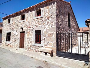 A stone building with a tiled roof, a gated entrance, and a small porch. - Country House 'Casa Rural El Robledo' with Private Terrace and Private Garden (Muñotello)