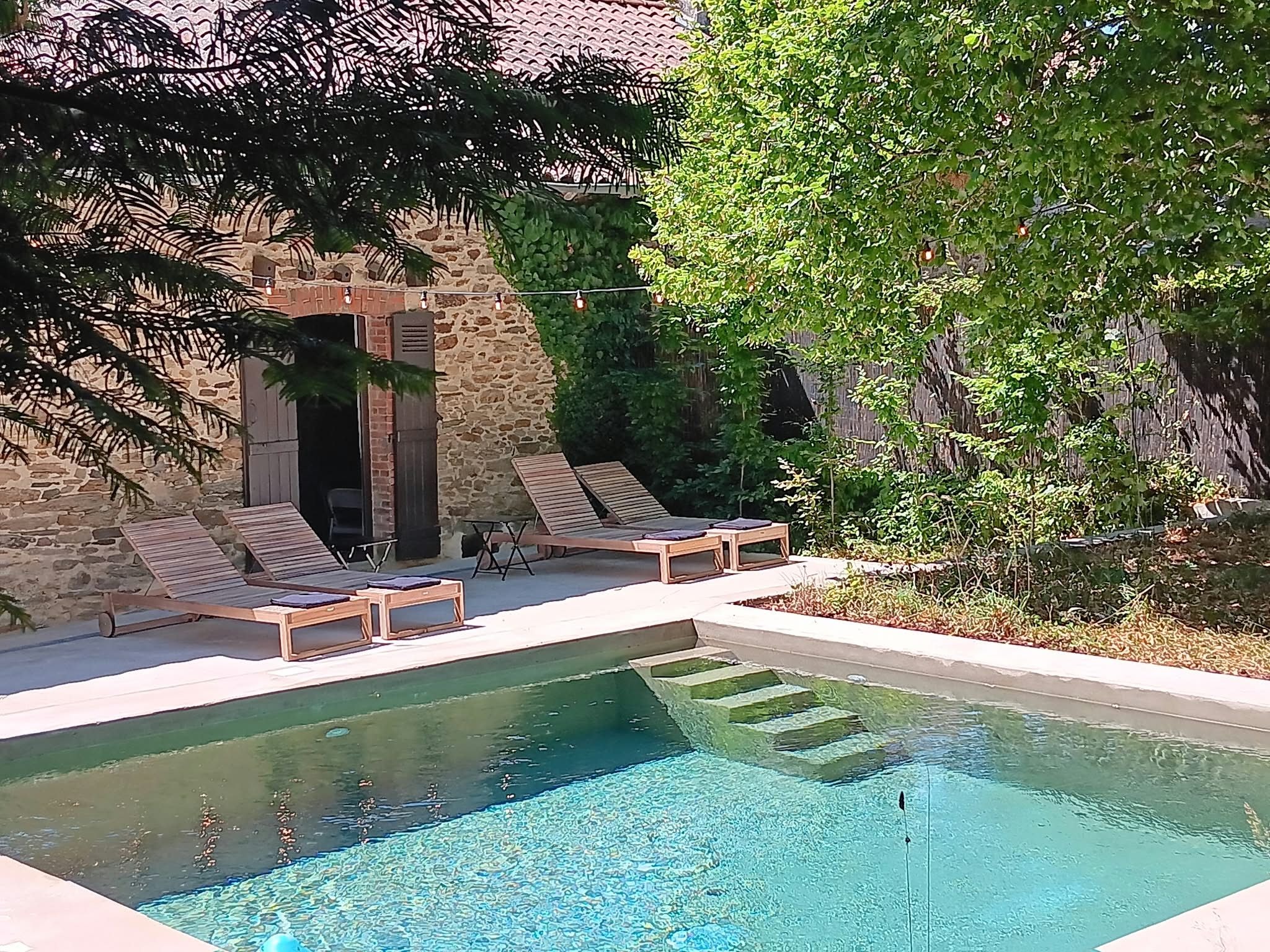 Un área de piscina con sillones de descanso y un edificio de piedra con un acceso abierto.