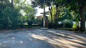 An outdoor area with stone flooring, surrounded by trees and greenery.