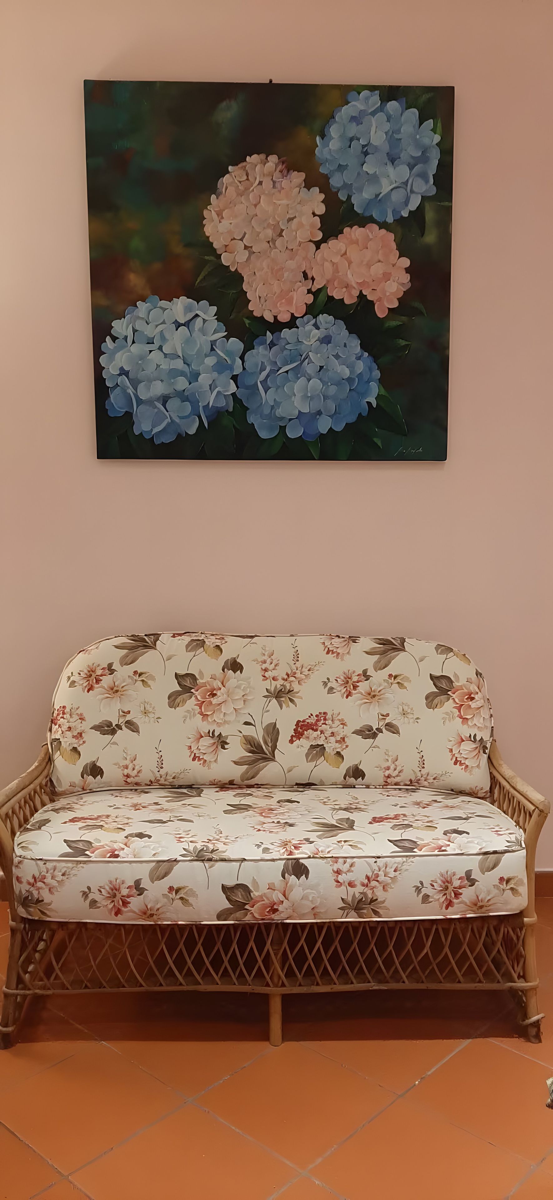Un canapé à motifs floraux, un mur orné d’un tableau représentant des fleurs et un sol carrelé.