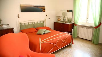 Une chambre à coucher comprenant un lit, une chaise, une table de chevet, une lampe, une fenêtre avec des rideaux et un radiateur.