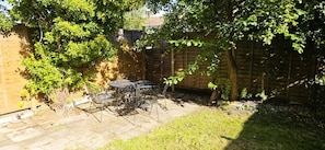 A backyard with a patio table and chairs, surrounded by a wooden fence and trees. - The Charlton Suite (Harrow)