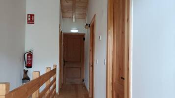 Un pasillo de madera con barandilla de madera, un extintor y una puerta al final.