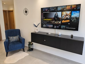 Un salon moderne avec un téléviseur à écran plat fixé sur une console noire, un fauteuil bleu et une horloge murale décorative.