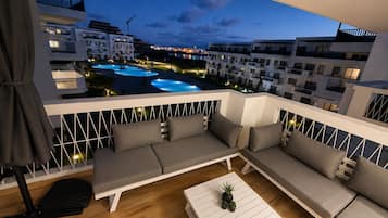 Un balcon avec un canapé et une table basse, donnant sur une piscine et des immeubles.