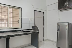 A kitchen with a built-in refrigerator, a window with a metal grill, and a door with a handle. - Hotel O Dazzling Studio (Pune)