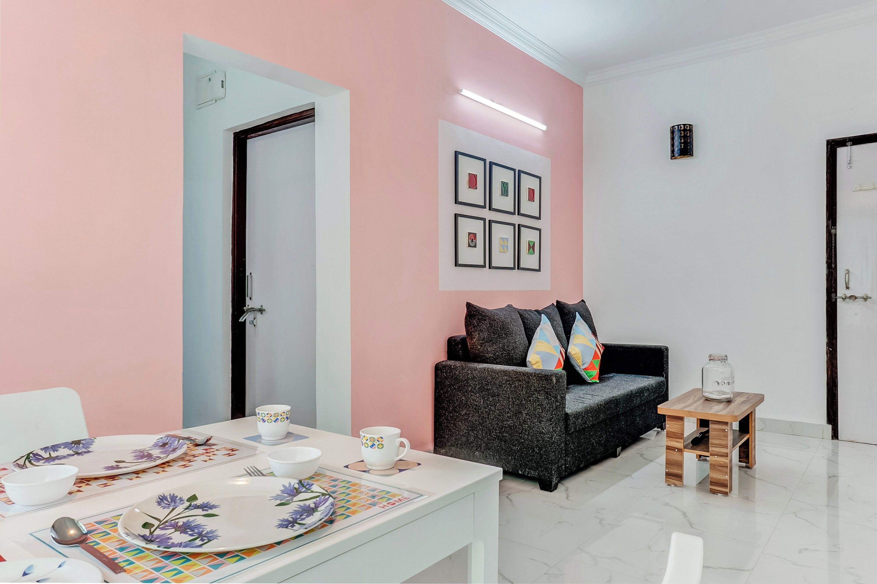 Ein Zimmer mit einem Esstisch, gedeckt mit Tellern, Tassen und Besteck. Es gibt ein Sofa mit Kissen und einen kleinen Holztisch mit einem Glas.