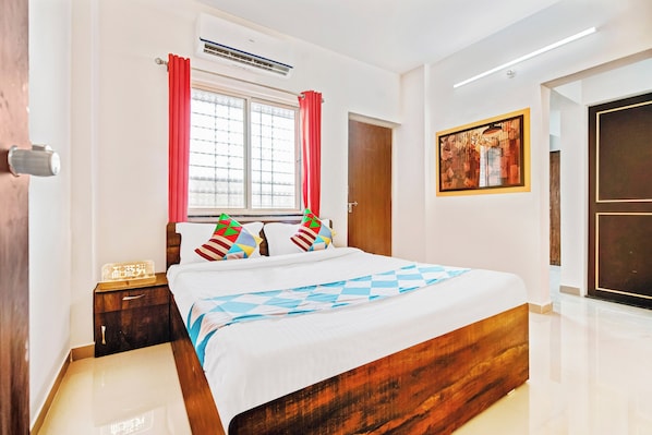 Una habitación de hotel con una cama, una mesita de noche, una ventana con cortinas, un equipo de aire acondicionado y una puerta.