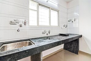 A kitchen with a marble countertop, a sink, and a window with blinds. - Hotel O Home Elegant RK Fursungi (Pune)