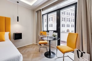 A hotel room with a bed, a desk, a chair, a table, and a large window with a view of buildings. - Glam44 Private Suites (ROMA)