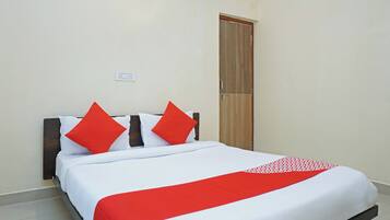 A bed with white bedding and red accents, a wooden door, and a wall socket.