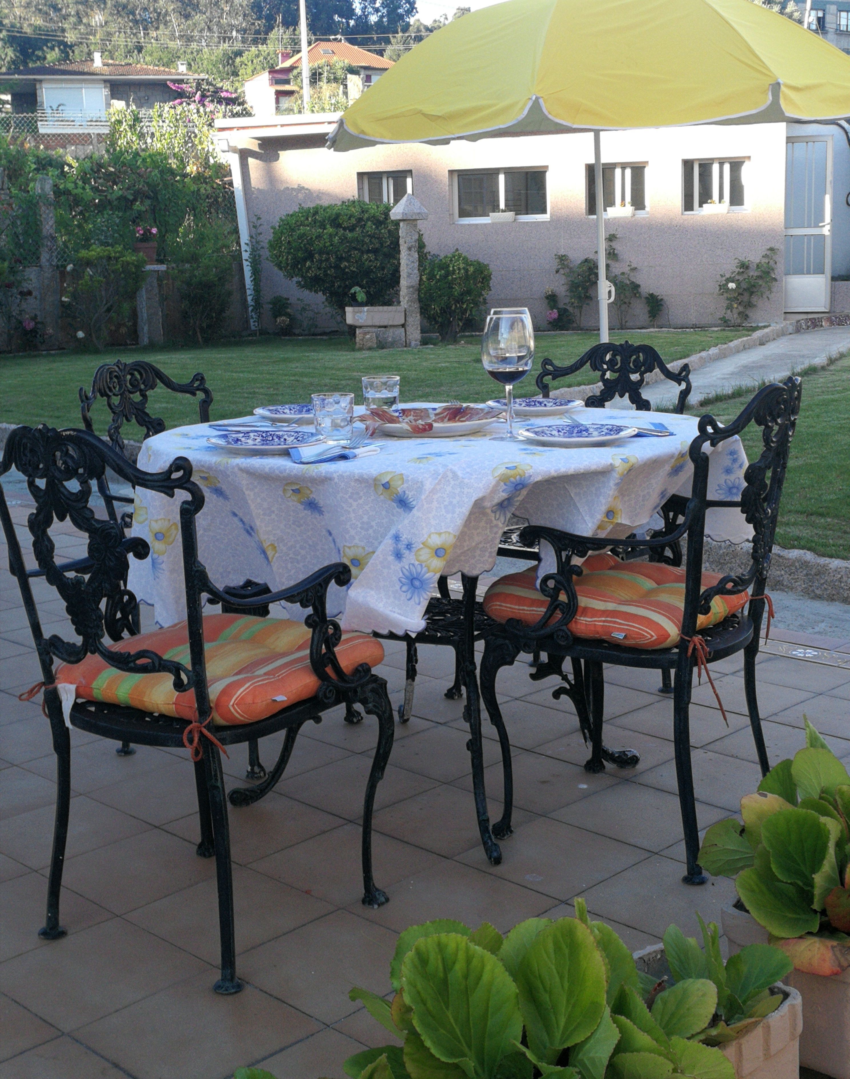 Un área de comedor al aire libre con una mesa dispuesta para cuatro personas, rodeada de sillas ornamentadas y cojines de colores.