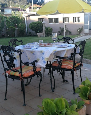 Un área de comedor al aire libre con una mesa dispuesta para cuatro personas, rodeada de sillas ornamentadas y cojines de colores.