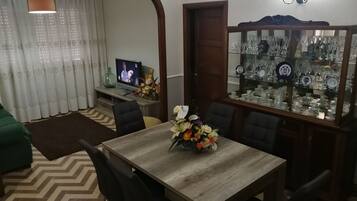 Un comedor con una mesa de madera, sillas, un televisor y un aparador de vidrio con vajilla.