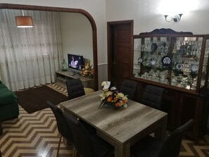 Un coin repas comprenant une table en bois, des chaises, un téléviseur et un meuble vitré contenant de la vaisselle.