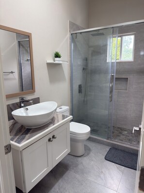 Un baño moderno con un lavamanos tipo recipiente, un inodoro y una ducha con cerramiento de vidrio.