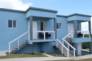 Un edificio de dos pisos con fachada azul, barandales blancos y una escalera que conduce a la entrada.