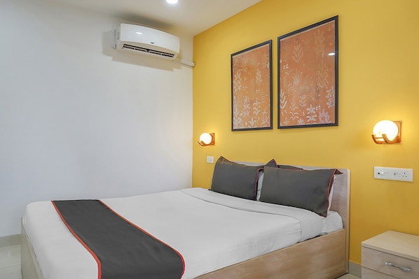 A hotel room with a bed, bedside tables, an air conditioning unit, and two wall-mounted light fixtures. - Hotel O by OYO Galaxy Hospitality (Pune)