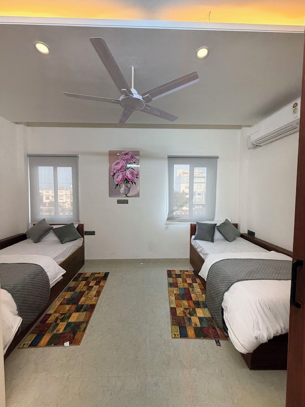 Habitación de hotel con dos camas, ventilador de techo, equipo de aire acondicionado y ventana con vistas.