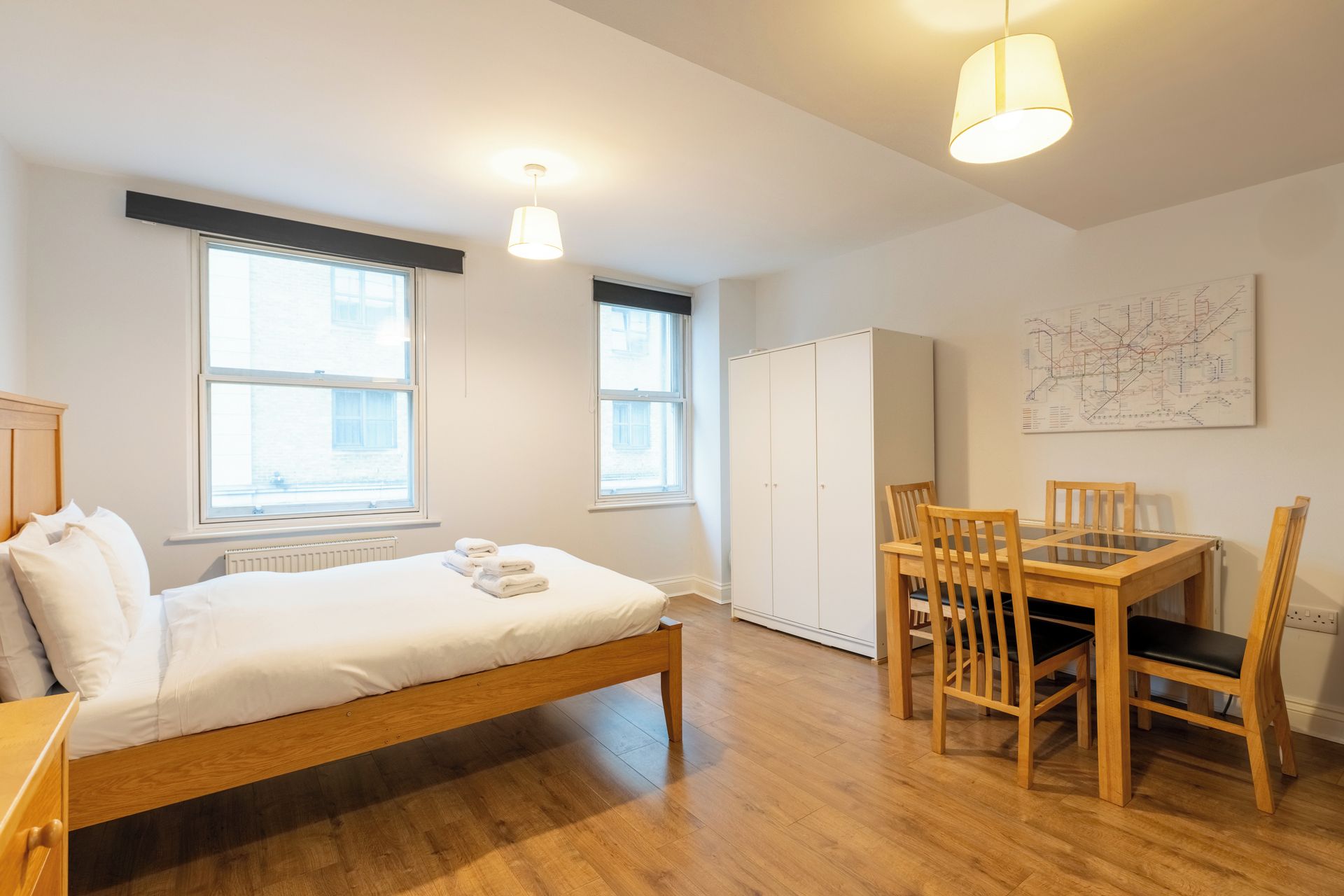 A bedroom with a bed, a wooden table with chairs, a wardrobe, and a window.