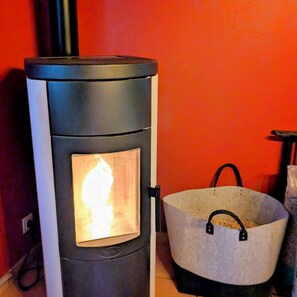 Ein Kaminofen mit sichtbarer Flamme, ein Aufbewahrungskorb und eine rote Wand im Hintergrund.