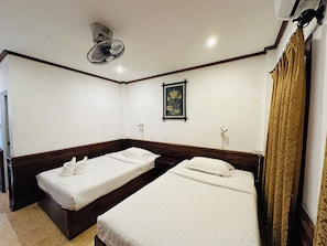 Ein Hotelzimmer mit zwei Einzelbetten, einem Deckenventilator, einem gerahmten Bild an der Wand und einem Fenster mit Vorhängen.