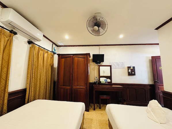 Ein Hotelzimmer mit zwei Betten, einem Schreibtisch, einem Spiegel, einem Fernseher und einem Kleiderschrank.