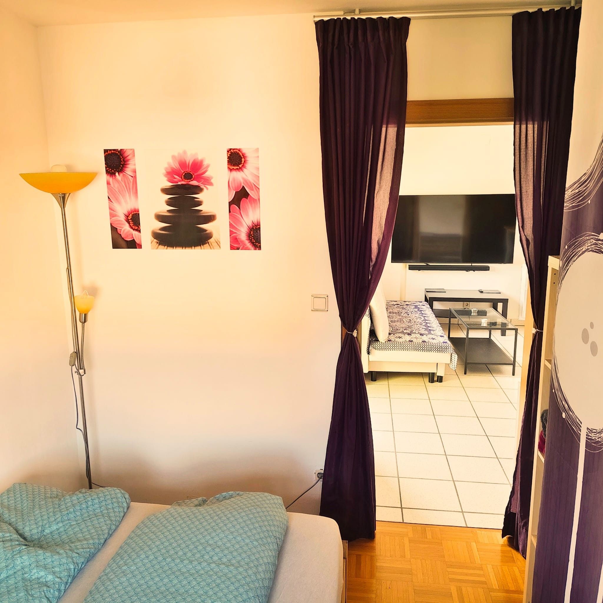 Een slaapkamer met een bed, een staande lamp en een televisie op de achtergrond.