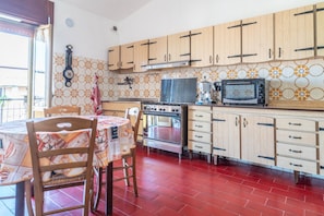 Una cocina con armarios de madera, estufa a gas, microondas y piso con baldosas rojas.