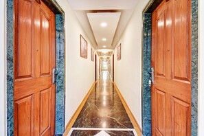 Un pasillo de hotel con puertas de madera, suelo de mármol y cuadros enmarcados en las paredes.