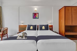 A hotel room with two beds, a wooden wardrobe, a desk with a kettle, and a colorful artwork on the wall. - Townhouse Hotel Golden Emerald (Pune)