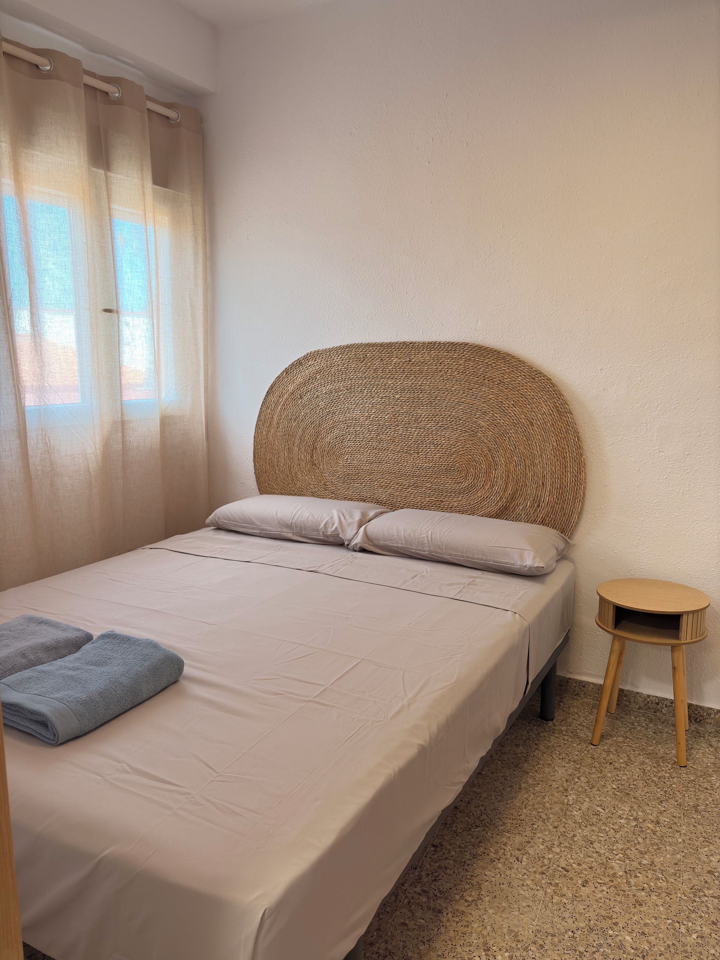 A single bed with a woven headboard, a small wooden nightstand, and a pair of folded towels.
