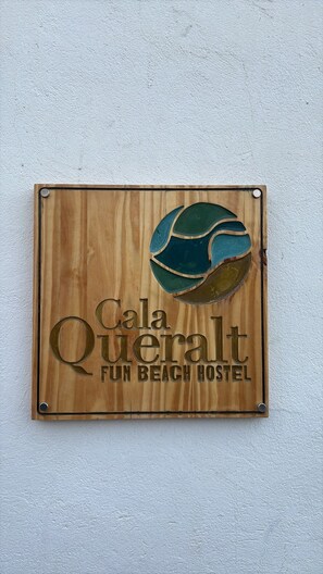 A wooden sign with the text 'Cala Queralto FUN BEACH HOSTEL' and a graphic of a beach ball. - Queralt Guest House (Sagunto)