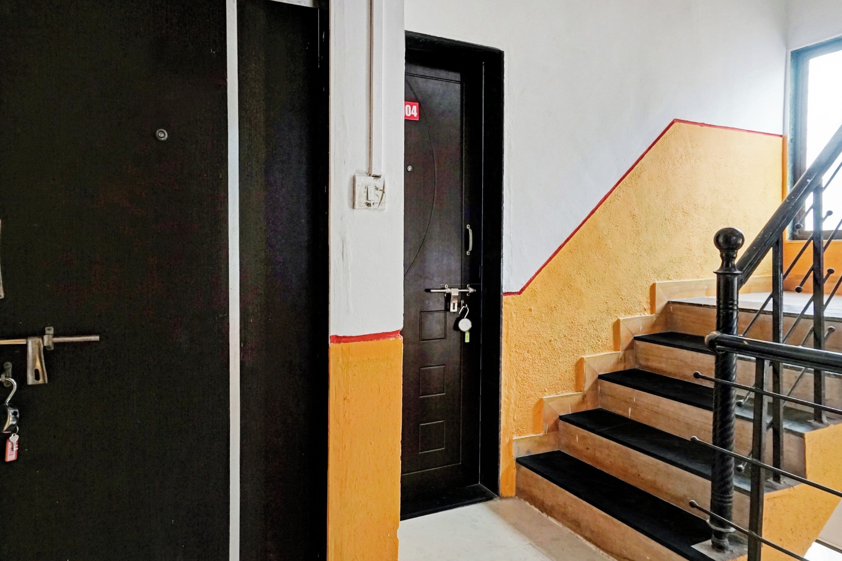 Una escalera con peldaños negros y amarillos, una puerta negra con un número rojo y una barandilla de metal.