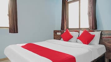 A bed with white and red bedding, a wooden headboard, and two windows with curtains.