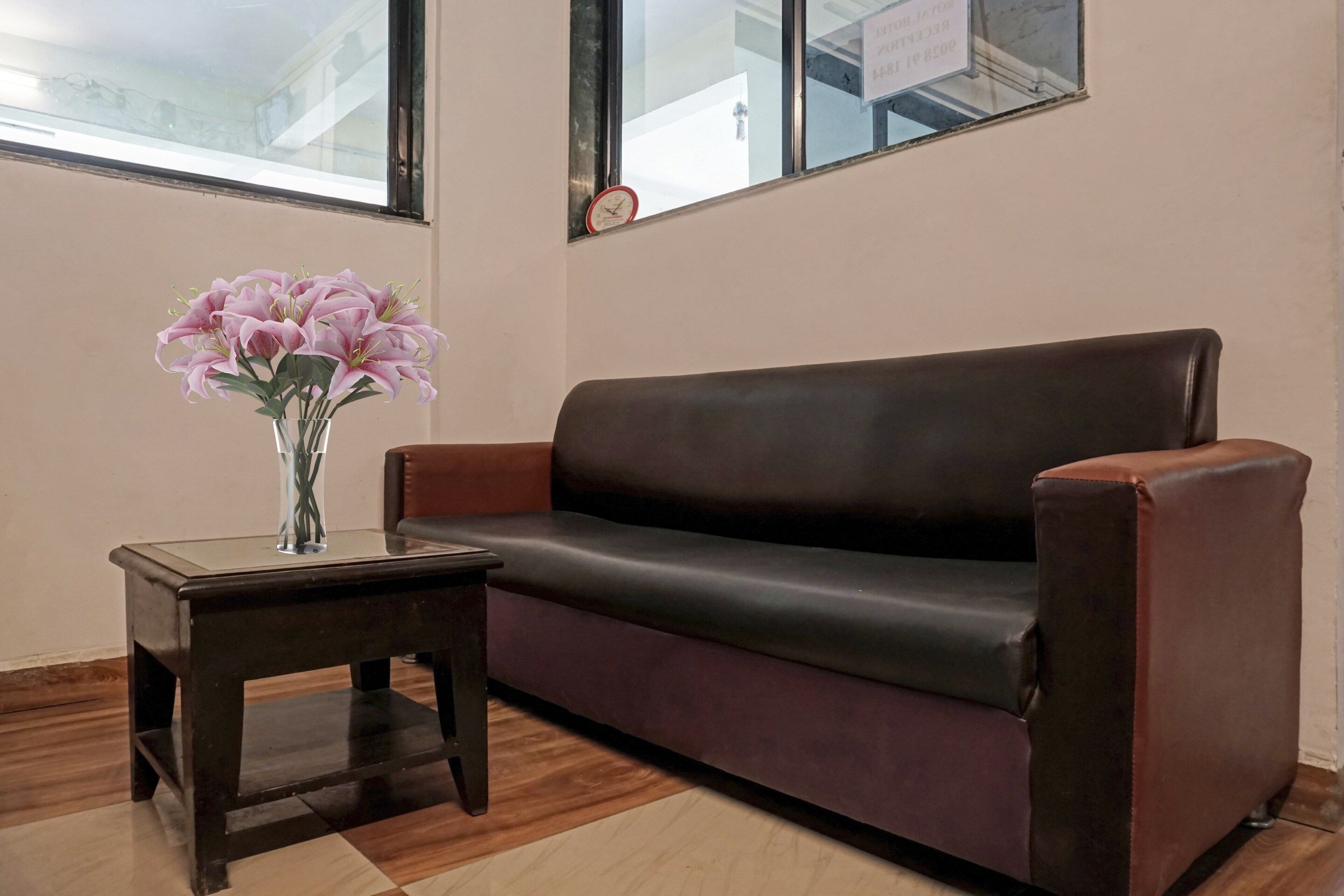 A room with a brown leather sofa, a small wooden side table, and a vase with flowers.