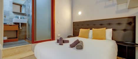A hotel room with a large bed, a nightstand, a bedside table, a bathroom with a sink, and a sliding glass door leading to an outdoor area.