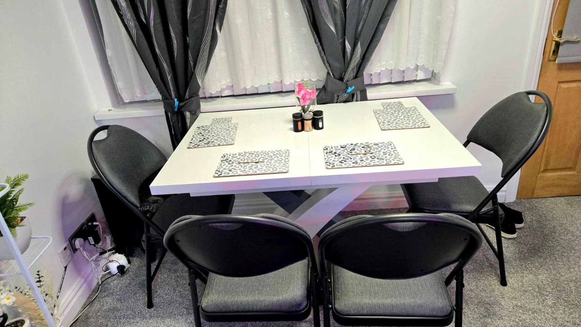 Una mesa de comedor con cuatro sillas, un florero con flores y una ventana con cortinas.