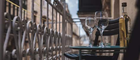 A table with two glasses and a bottle, set against a backdrop of a metal fence and buildings.
