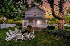 Una casa blanca con porche, mobiliario exterior y un árbol grande.