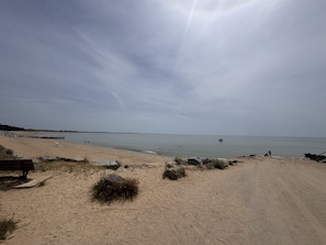 En strand med en sandstig som leder ner till vattnet, en bänk och en klippformation.