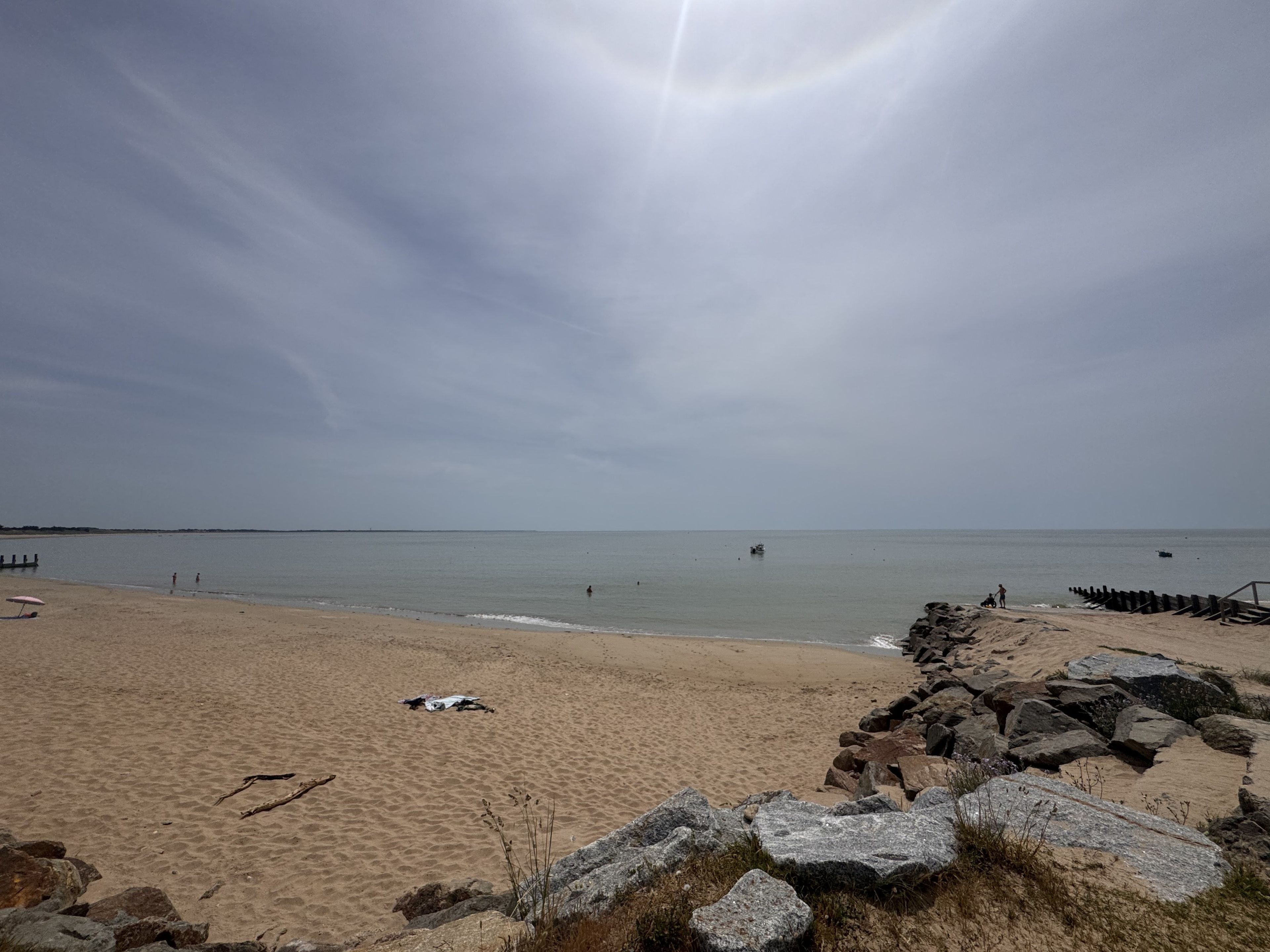 En strand med sandet bredde, en stenbrydning og roligt hav.