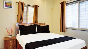 A bedroom with a bed, curtains, a nightstand, a vase with flowers, and a wall-mounted picture.
